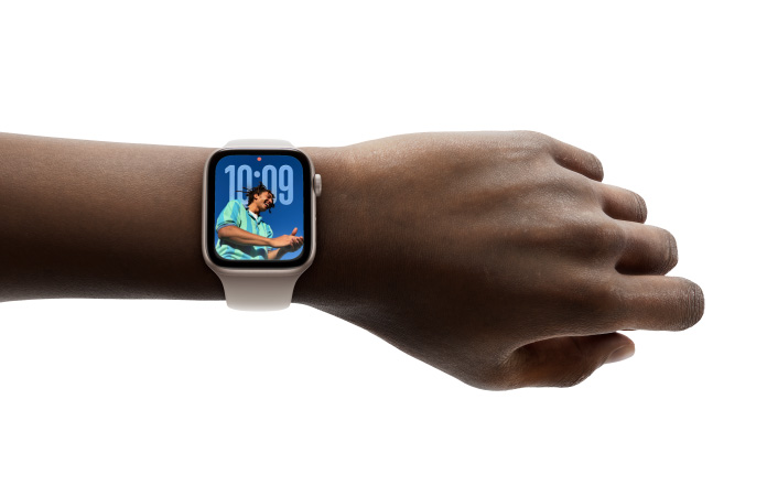 Close-up of Apple Watch in Rose Gold with rubber band on a person’s wrist, showing Time app in new Liquid Glass design