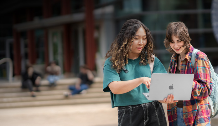 Dos estudiantes universitarios miran la pantalla de un MacBook en el campus