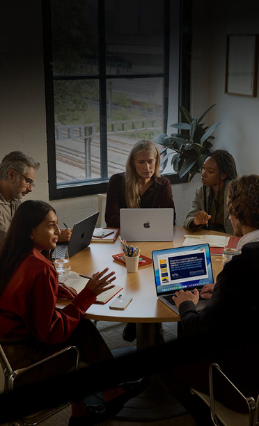 Fünf Personen sitzen an einem Konferenztisch und arbeiten zusammen an MacBooks, während ihre iPhones umgedreht auf dem Tisch liegen
