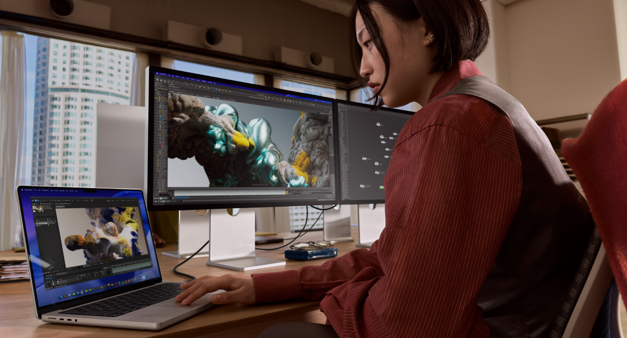 Osoba v kancelárii pracuje na MacBooku, ku ktorému je cez port Thunderbolt 5 pripojený Studio Display XDR