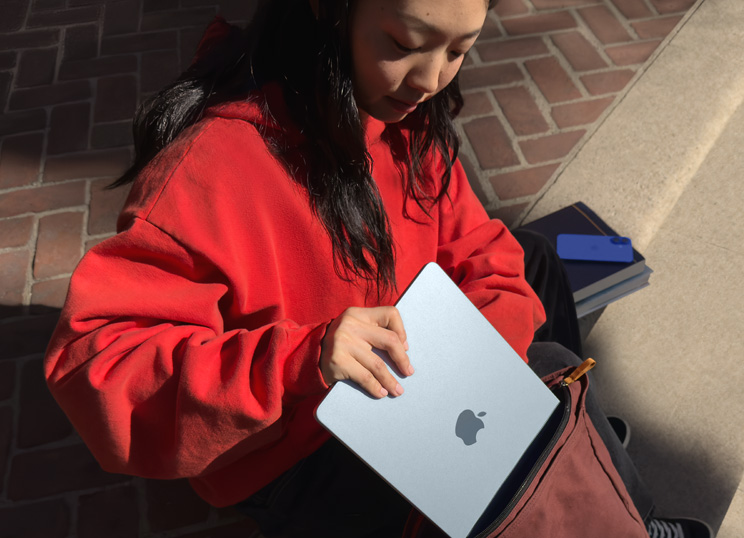 Une personne assise sur des marches en pierre range un MacBook dans un sac à dos.