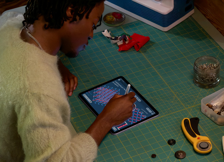 Une personne réalisant une illustration sur iPad avec un Apple Pencil, installée devant un tapis de découpe vert avec du matériel de couture.