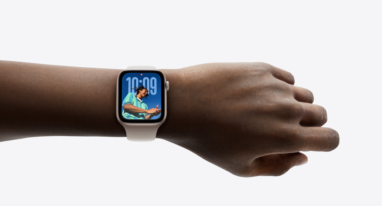 Zbliżenie na nadgarstek z zegarkiem Apple Watch w kolorze srebrnym z gumowym paskiem. Na zegarku można podziwiać nowy dizajn aplikacji Czas z wykorzystaniem technologii Liquid Glass.